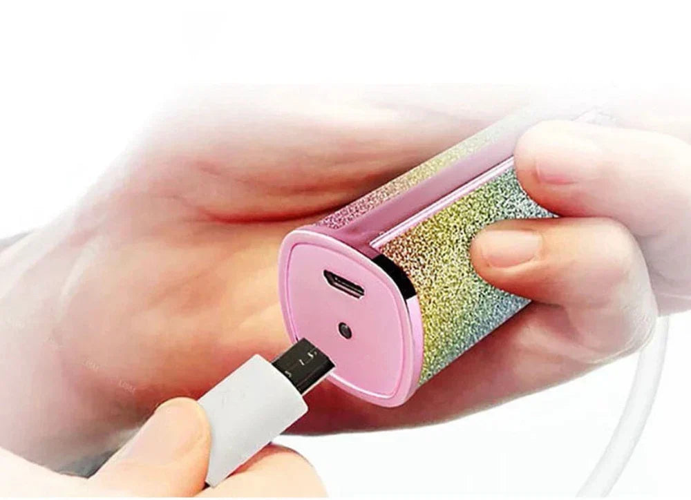A person charging a pink glittery AVIOX precision eyebrow trimmer via USB.